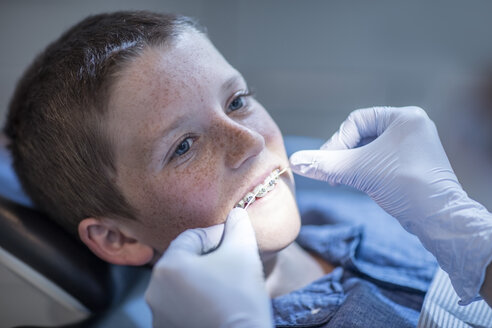 Boy with braces in dental surgery receiving dental floss treatment - ZEF10651