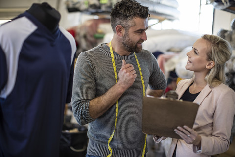 Schneiderin im Gespräch mit Frau mit Klemmbrett in der Werkstatt, lizenzfreies Stockfoto