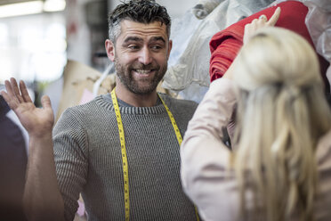 Smiling tailor looking at fashion designer in workshop - ZEF10674