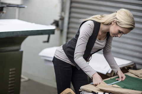 Junge Frau bei der Arbeit mit einem Maßband in einer Schneiderei, lizenzfreies Stockfoto