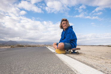 Spanien, Teneriffa, lächelnder Junge sitzt auf seinem Skateboard am Straßenrand - SIPF00944