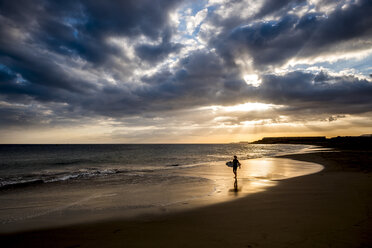 Spain, Tenerife, boy carrying surfboard on the beach at sunset - SIPF00957