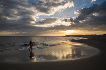 Spain, Tenerife, boy carrying surfboard on the beach at sunset - SIPF00959