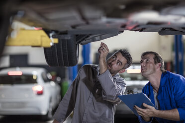 Zwei Automechaniker in einer Werkstatt, die gemeinsam ein Auto untersuchen - ZEF10702