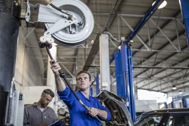 Automechaniker in einer Werkstatt beim Ziehen an einer Schlauchmaschine - ZEF10708