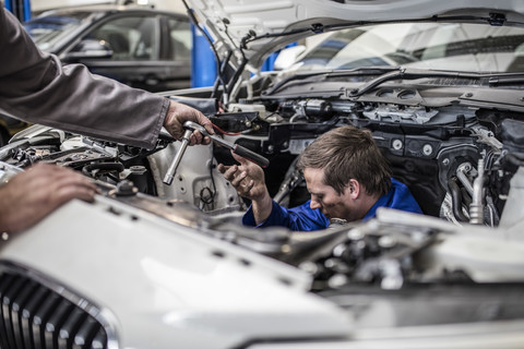 Zwei Automechaniker in einer Werkstatt reparieren gemeinsam ein Auto, lizenzfreies Stockfoto