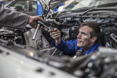 Zwei Automechaniker in einer Werkstatt reparieren gemeinsam ein Auto, lizenzfreies Stockfoto