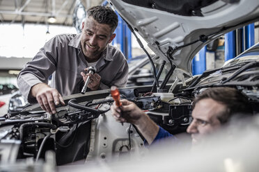 Two car mechanics in a workshop repairing car together - ZEF10726