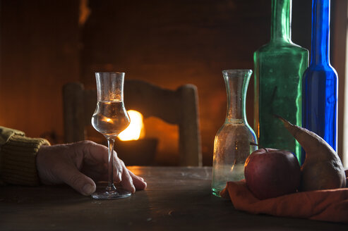 Hand mit Schnapsglas und Flaschen vor einem offenen Feuer - HHF05453