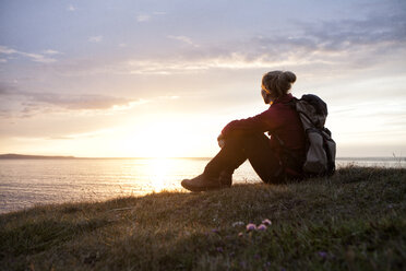 Island, Wanderer sitzt auf einer Wiese und betrachtet die Aussicht in der Dämmerung - RBF05213