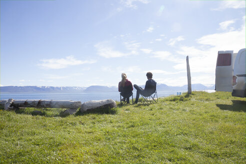Island, Rückenansicht eines Paares, das auf Campingstühlen sitzt und die Aussicht betrachtet - RBF05223