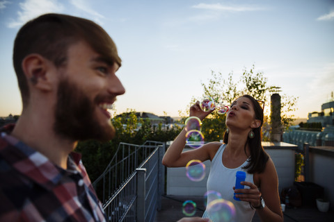 Junge Frau bläst Seifenblasen auf der Dachterrasse, lizenzfreies Stockfoto