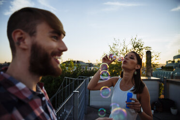 Young woman blowing soap bubbles on roof terrace - AIF00406