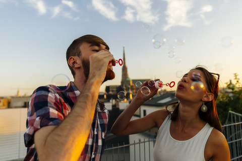 Österreich, Wien, junges Paar bläst Seifenblasen auf Dachterrasse, lizenzfreies Stockfoto