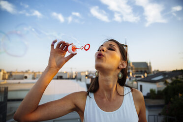 Austria, Vienna, young woman blowing soap bubbles on roof terrace - AIF00410