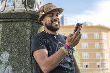 Porträt eines lächelnden Mannes, der auf sein Smartphone schaut - TAMF00697