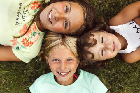 Three smiling girls lying head to head on a meadow stock photo