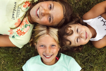 Drei lächelnde Mädchen liegen Kopf an Kopf auf einer Wiese - MGOF02545