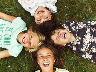 Vier lachende Mädchen liegen Kopf an Kopf auf einer Wiese - MGOF02549