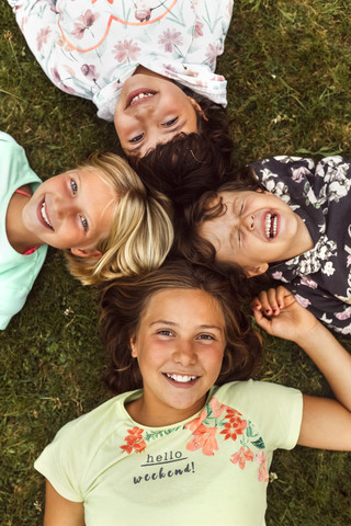 Four laughing girls lying head to head on a meadow stock photo