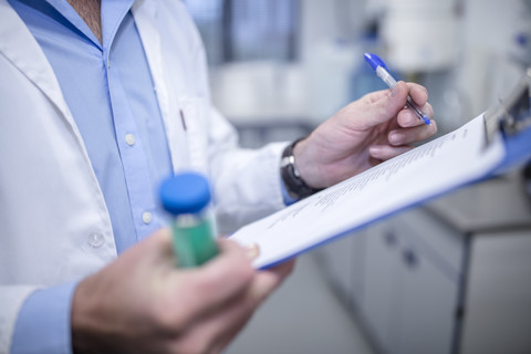 Wissenschaftlerin mit Klemmbrett und Reagenzglas bei der Arbeit im Labor, lizenzfreies Stockfoto