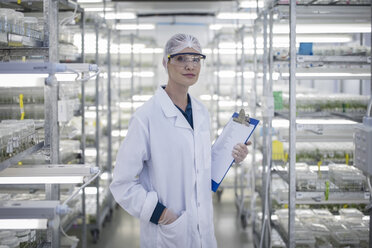 Smiling woman wearing protective clothing in lab holding clipboard - ZEF10845