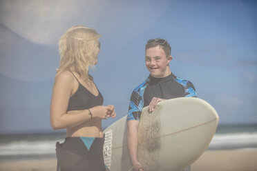 Teenage boy with down syndrome and woman with surfboard on beach - ZEF10865