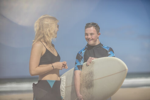Teenage boy with down syndrome and woman with surfboard on beach - ZEF10865