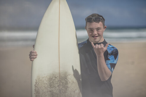 Teenage boy with down syndrome with surfboard on beach - ZEF10866