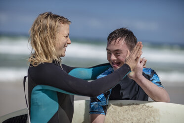 Happy teenage boy with down syndrome and woman with surfboard on beach - ZEF10874