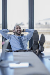 Smiling businessman sitting at his desk with feet up - ZEF10959