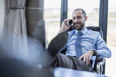 Smiling businessman sitting at his desk, talking on the phone - ZEF10960