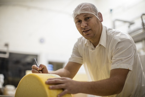 Arbeiter in einer Käsefabrik beim Etikettieren eines Käselaibs, lizenzfreies Stockfoto