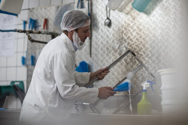 Arbeiter in einer Käsefabrik reinigt Behälterteile - ZEF11055