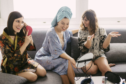 Three young women sitting on the couch wearing bathrobes preparing for the day - LCUF00066