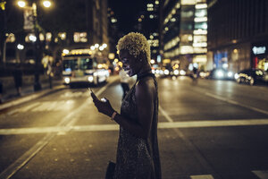 USA, New York City, smiling young woman on Times Square at night looking at cell phone - GIOF01567