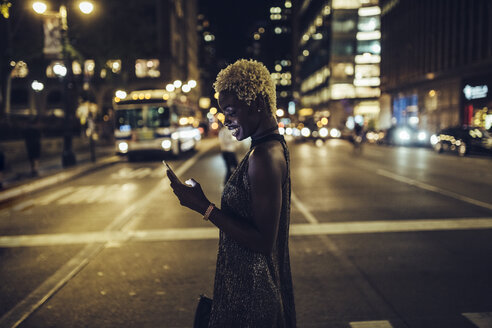 USA, New York City, lächelnde junge Frau auf dem Times Square bei Nacht, die auf ihr Handy schaut - GIOF01567