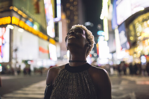 USA, New York City, lächelnde junge Frau auf dem Times Square bei Nacht, die nach oben schaut - GIOF01570