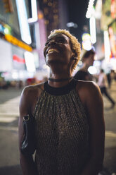 USA, New York City, lächelnde junge Frau auf dem Times Square bei Nacht, die nach oben schaut - GIOF01571