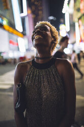 USA, New York City, smiling young woman on Times Square at night looking up - GIOF01571