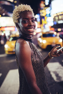 USA, New York City, Porträt einer lächelnden jungen Frau auf dem Times Square bei Nacht - GIOF01576