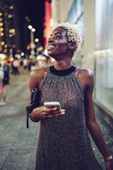 USA, New York City, lächelnde junge Frau auf dem Times Square bei Nacht, die etwas beobachtet - GIOF01577