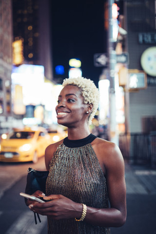 USA, New York City, lächelnde junge Frau wartet nachts auf dem Times Square, lizenzfreies Stockfoto