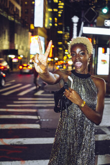 USA, New York City, junge Frau mit Siegeszeichen auf dem Times Square bei Nacht - GIOF01582