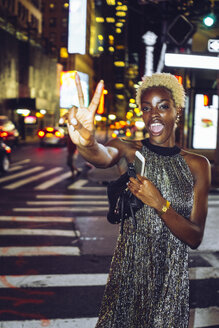 USA, New York City, young woman showing victory sign on Times Square at night - GIOF01582