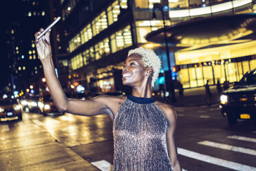 USA, New York City, smiling young woman on Times Square at night taking selfie - GIOF01587
