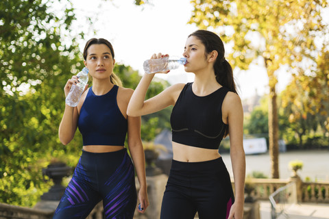 Zwei sportliche junge Frauen trinken aus Flaschen, lizenzfreies Stockfoto