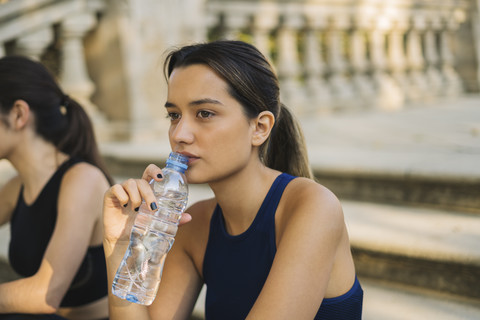 Sportliche junge Frau sitzt auf einer Treppe und trinkt aus einer Flasche, lizenzfreies Stockfoto