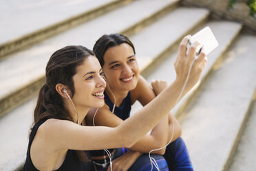 Zwei sportliche junge Frauen sitzen auf einer Treppe und machen ein Selfie - EBSF01795