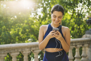 Sportive young woman with earbuds looking at cell phone - EBSF01798